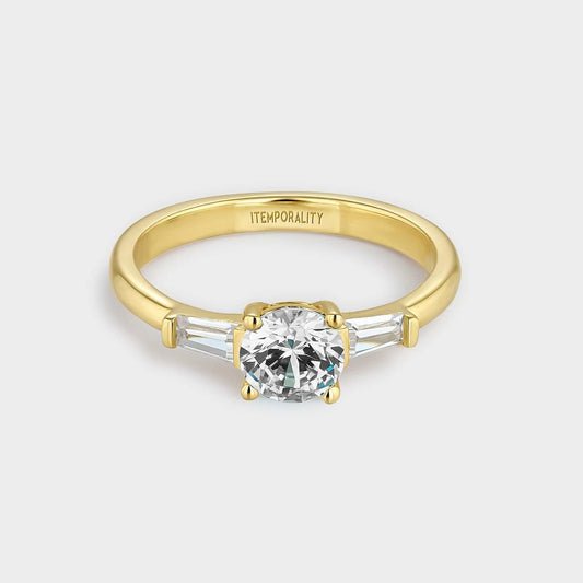 Gelbvergoldeter Silberring mit zwei weißen rechteckigen Zirkonen und einem größeren weißen runden zentralen Zirkon.