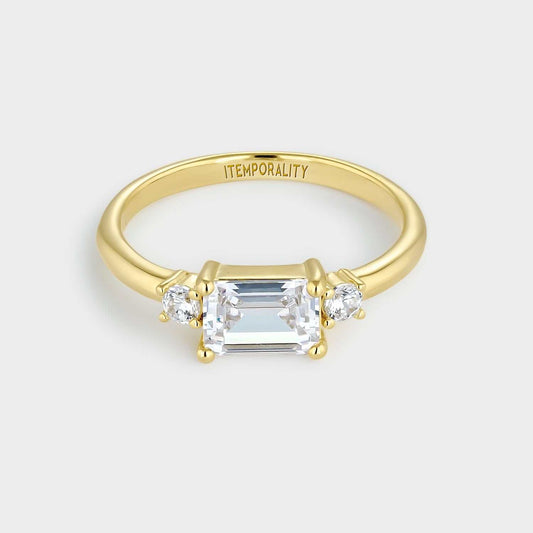 Anillo de plata bañada en oro amarillo con circonita central blanca rectangular engastada en cuatro garras y dos circonitasa  redondas blancas a ambos lados