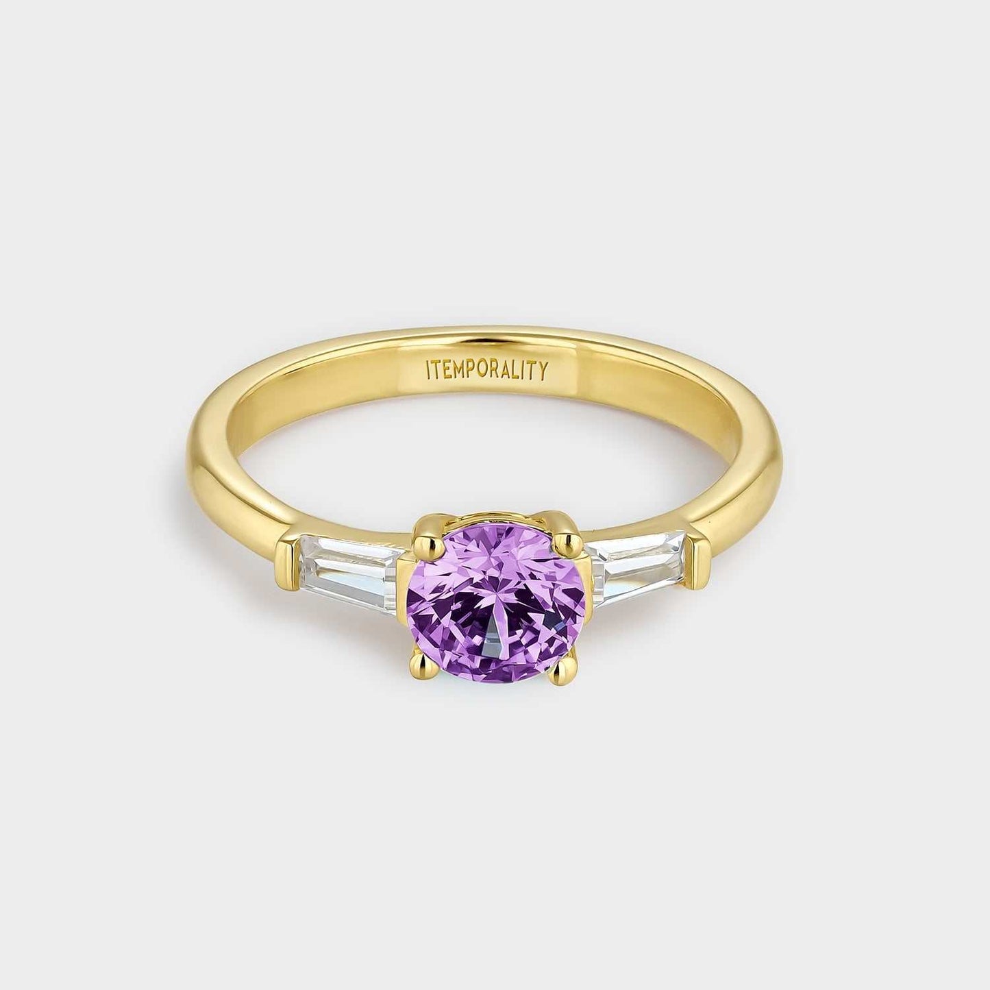 Anillo de plata bañada en oro amarillo con dos circonitas blancas rectangulares y circonita central redonda de mayor tamaño color amatista.